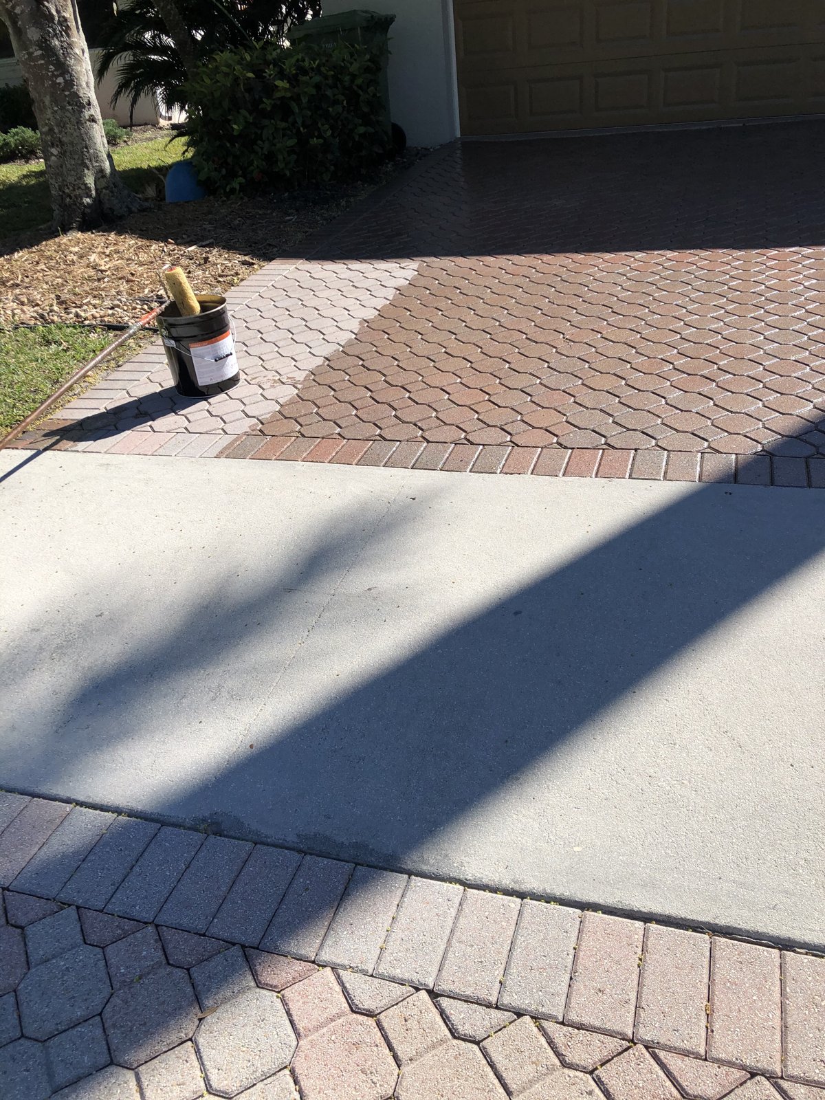Sealer going down on a paver driveway in South Florida — rich color on the sealed side, dull pavers still to seal